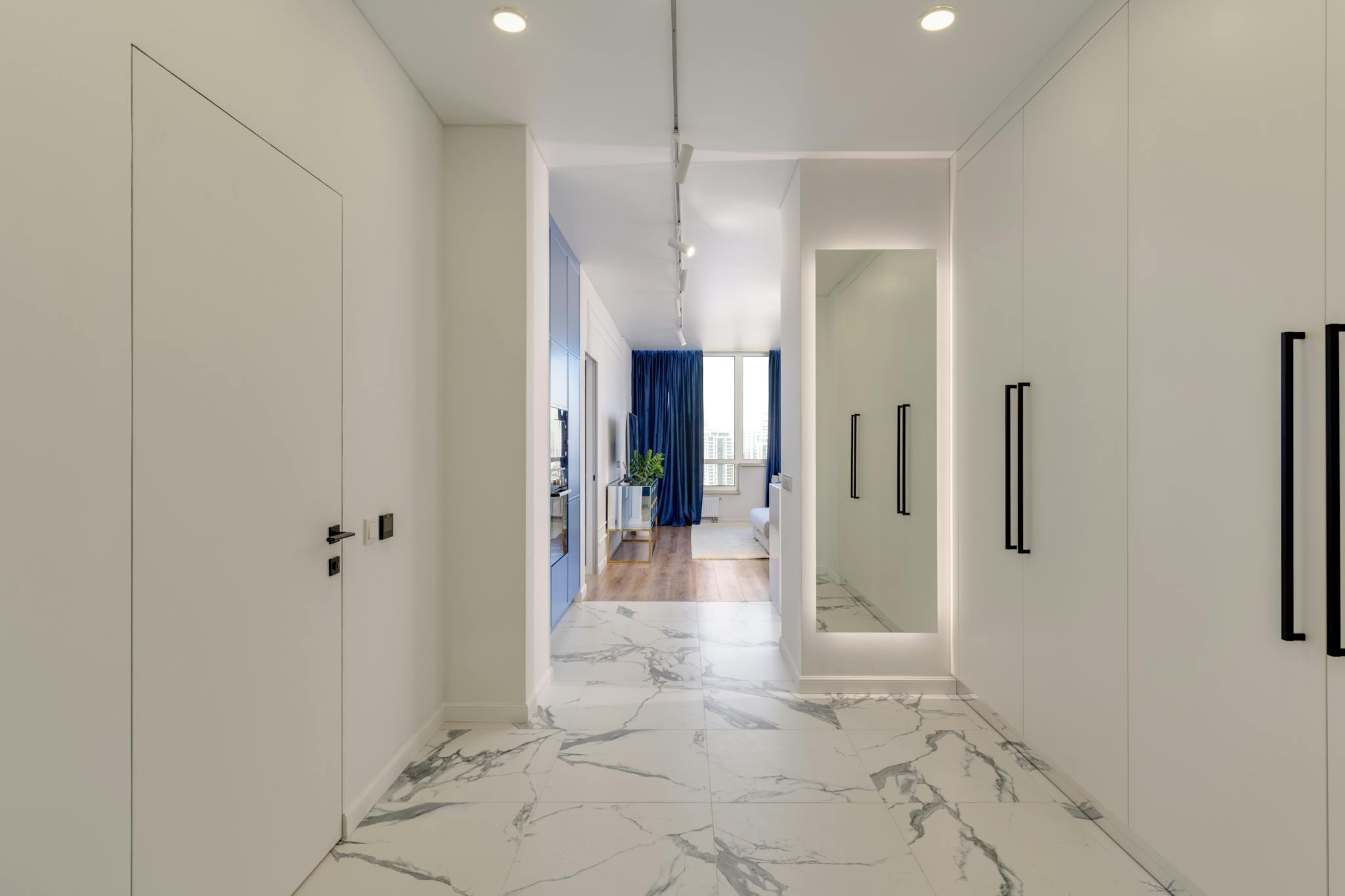 A bright corridor with marble flooring leading to a living area, featuring a mirror and sleek design.